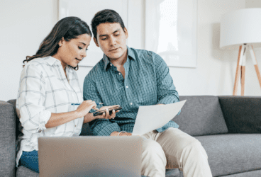 Couple calculating tax offset benefits with smartphone and documents in a cozy living room.