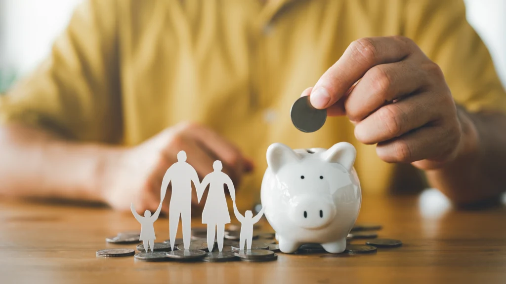 Person popping coins into a piggy bank with a family cut-out, representing saving money for their family