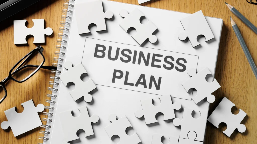 Business plan folio surrounded by puzzle pieces on a desk with stationary